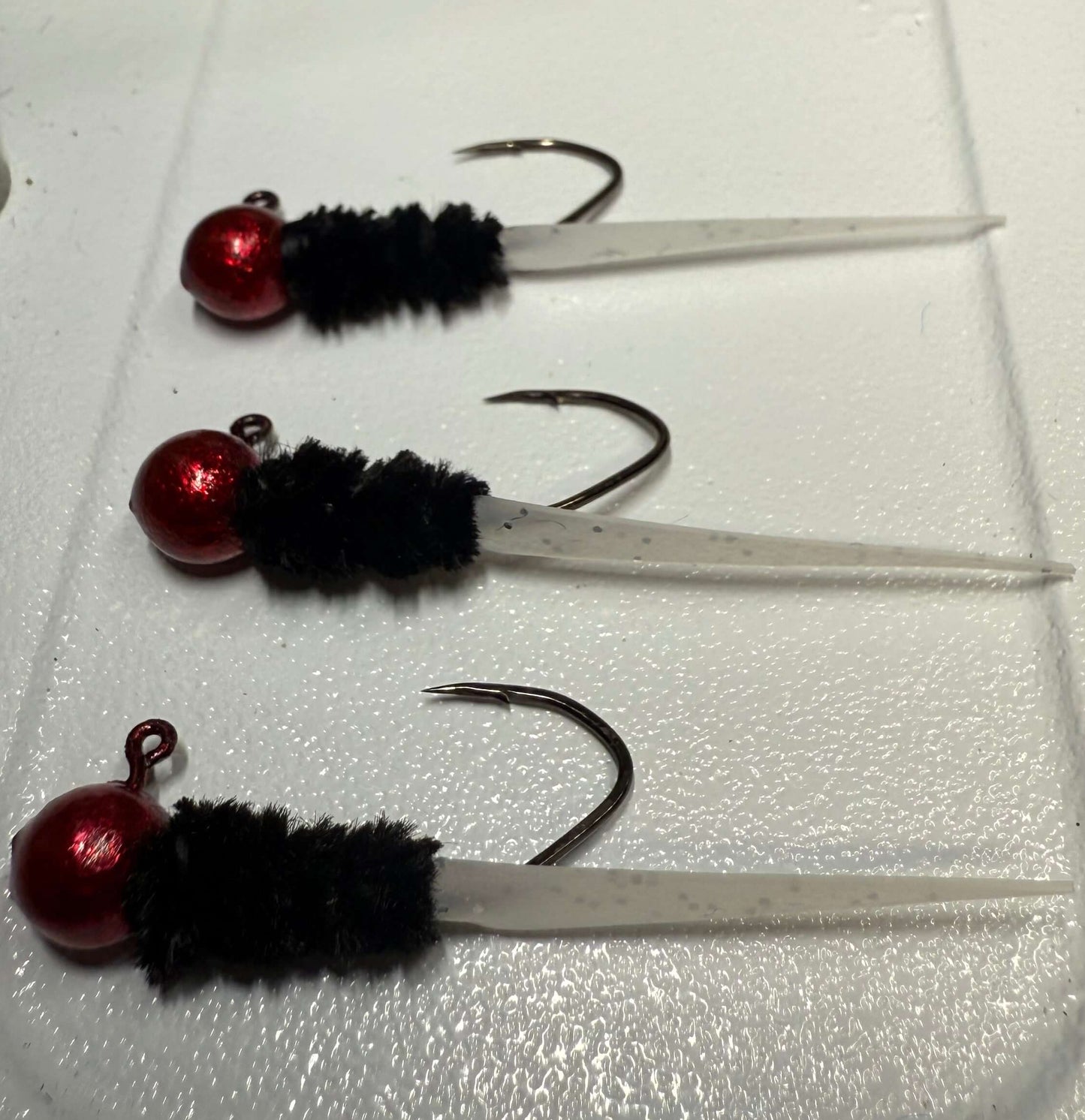 Hand tied Crappie jigs with red beads and #4 sickle hooks on a white surface, ideal for Crappie fishing.